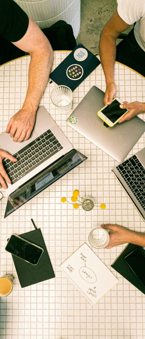 Top view of a team collaborating with laptops, phones, and notes in a modern office.